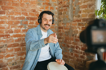 Image showing Caucasian musician playing hand drum during online concert at home isolated and quarantined, smiling, talking to audience