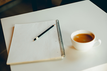 Image showing White cup of hot coffee and white sketch book on the table - working process, inspiring workplace