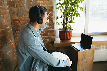 Image showing Caucasian musician playing hand drum during online concert at home isolated and quarantined, greeting band or audience