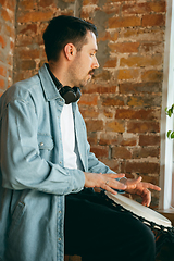 Image showing Caucasian musician playing hand drum during online concert at home isolated and quarantined, inspired improvising