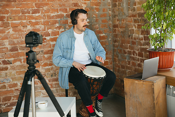 Image showing Caucasian musician playing hand drum during online concert at home isolated and quarantined, inspired improvising