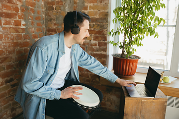 Image showing Caucasian musician playing hand drum during online concert at home isolated and quarantined, inspired improvising