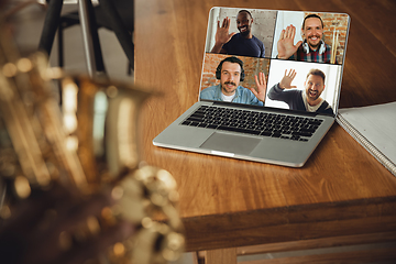 Image showing African-american musician playing saxophone during online concert or sound-check connected with the band at home quarantined, focus on laptop