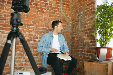 Image showing Caucasian musician playing hand drum during online concert at home isolated and quarantined, improvising