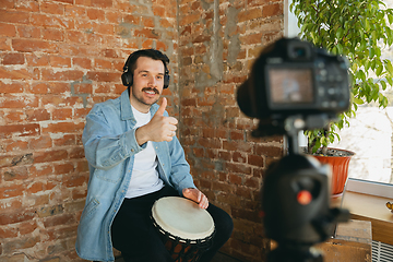 Image showing Caucasian musician playing hand drum during online concert at home isolated and quarantined, smiling, thumb up