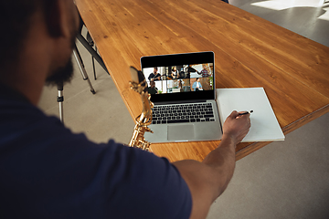 Image showing African-american musician playing saxophone during online concert or sound-check connected with the band at home isolated and quarantined