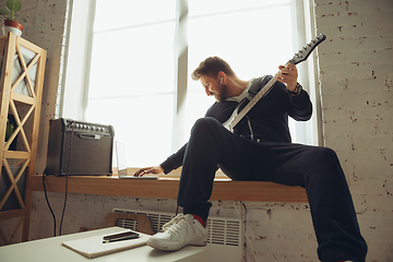 Image showing Caucasian musician playing guitar during online concert at home isolated and quarantined, tuning the stream