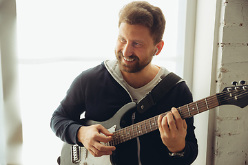 Image showing Caucasian musician playing guitar during online concert at home isolated and quarantined, cheerful improvising