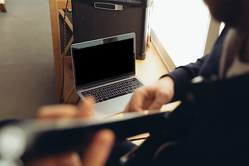 Image showing Caucasian musician playing guitar during concert at home isolated and quarantined, cheerful improvising, focus on blank laptop screen