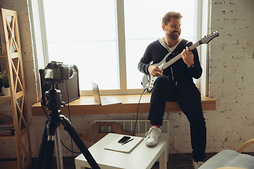 Image showing Caucasian musician playing guitar during online concert at home isolated and quarantined, cheerful improvising