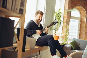 Image showing Caucasian musician playing guitar during online concert at home isolated and quarantined, cheerful improvising