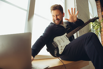 Image showing Caucasian musician playing guitar during concert at home isolated and quarantined, cheerful improvising with the band connected online