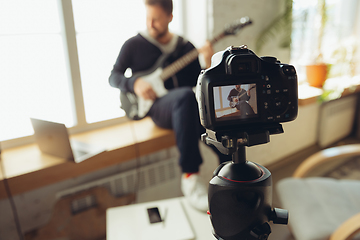 Image showing Caucasian musician playing guitar during concert at home isolated and quarantined, cheerful improvising, focus on camera