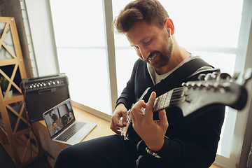 Image showing Caucasian musician playing guitar during concert at home isolated and quarantined, cheerful improvising with the band connected online