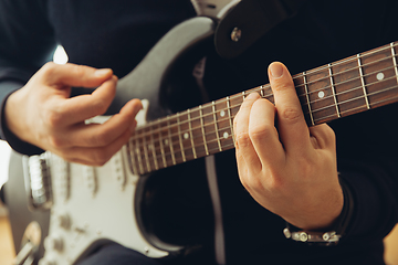 Image showing Caucasian musician playing guitar during concert at home isolated and quarantined, cheerful improvising, close up