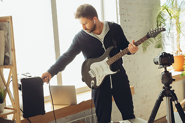 Image showing Caucasian musician playing guitar during online concert at home isolated and quarantined, tuning the stream