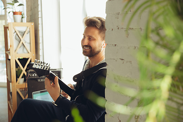 Image showing Caucasian musician playing guitar during online concert at home isolated and quarantined, cheerful improvising