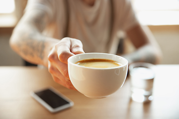 Image showing Close up of male hands proposing cup of coffee, sitting at the table with smartphone