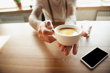 Image showing Close up of male hands proposing cup of coffee, sitting at the table with smartphone