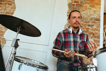 Image showing Caucasian musician playing drumms during online concert with the band at home isolated and quarantined, smiling, cheerful