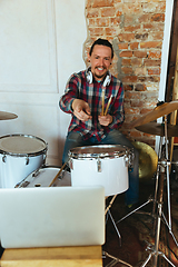 Image showing Caucasian musician playing drumms during online concert with the band at home isolated and quarantined, greeting audience