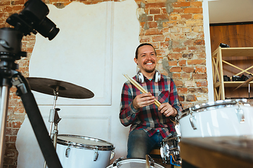 Image showing Caucasian musician playing drumms during online concert with the band at home isolated and quarantined, greeting audience