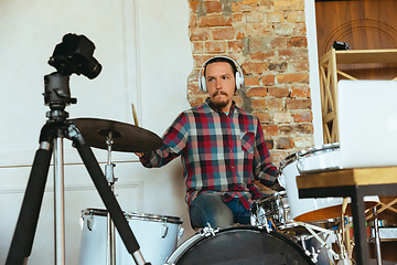 Image showing Caucasian musician playing drumms during online concert with the band at home isolated and quarantined, inspired improvising