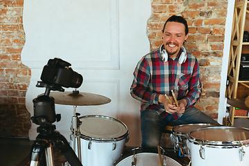 Image showing Caucasian musician playing drumms during online concert with the band at home isolated and quarantined, smiling, cheerful