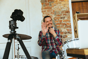 Image showing Caucasian musician playing drumms during online concert with the band at home isolated and quarantined, greeting audience