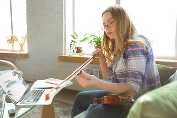 Image showing Young woman studying at home during online courses or free information by herself, playing violin, improvising