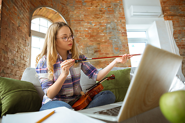 Image showing Young woman studying at home during online courses or free information by herself, playing violin, improvising