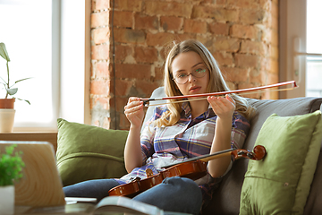 Image showing Young woman studying at home during online courses or free information by herself, playing violin, improvising