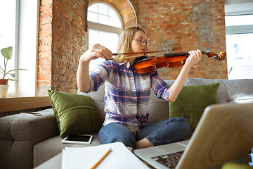 Image showing Young woman studying at home during online courses or free information by herself, playing violin, improvising