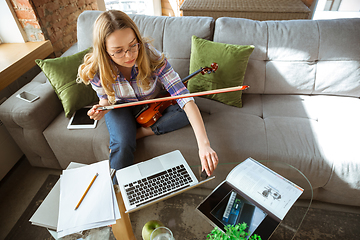 Image showing Young woman studying at home during online courses or free information by herself, playing violin, improvising