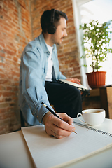 Image showing Caucasian musician playing hand drum during online concert at home isolated and quarantined, making notes, focus on hand