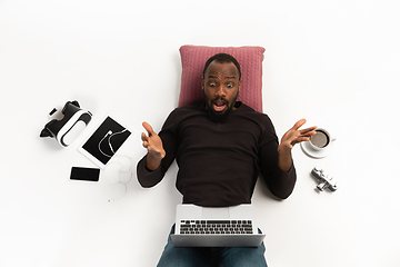 Image showing Emotional african-american man using laptop surrounded by gadgets isolated on white studio background, technologies. Shocked