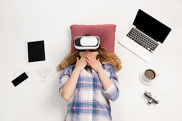 Image showing Emotional caucasian woman using VR-headsed, surrounded by gadgets isolated on white studio background, technologies. Shocked, scared