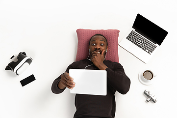 Image showing Emotional african-american man using tablet surrounded by gadgets isolated on white studio background, technologies connecting people. Shocked, scared