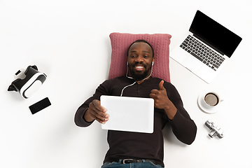 Image showing Emotional african-american man using tablet surrounded by gadgets isolated on white studio background, technologies connecting people. Smiling, thumb up