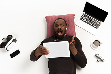 Image showing Emotional african-american man using tablet surrounded by gadgets isolated on white studio background, technologies. Angry asking