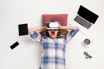 Image showing Emotional caucasian woman using VR-headsed, surrounded by gadgets isolated on white studio background, technologies. Shocked, scared