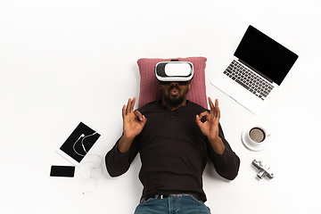 Image showing Emotional african-american man using VR-headset surrounded by gadgets isolated on white studio background, technologies. Nice, happy