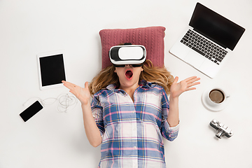 Image showing Emotional caucasian woman using VR-headsed, surrounded by gadgets isolated on white studio background, technologies. Shocked