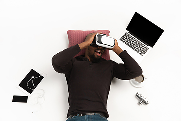 Image showing Emotional african-american man using VR-headset surrounded by gadgets isolated on white studio background, technologies. Emotional playing