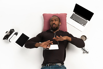 Image showing Emotional african-american man using phone surrounded by gadgets isolated on white studio background, technologies connecting people. Inspired singing