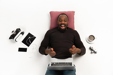 Image showing Emotional african-american man using laptop surrounded by gadgets isolated on white studio background, technologies. Showing thumbs up