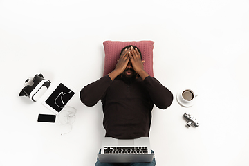 Image showing Emotional african-american man using laptop surrounded by gadgets isolated on white studio background, technologies. Shocked