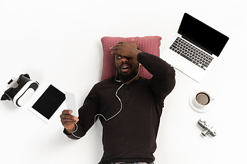 Image showing Emotional african-american man using phone surrounded by gadgets isolated on white studio background, technologies. Shocked