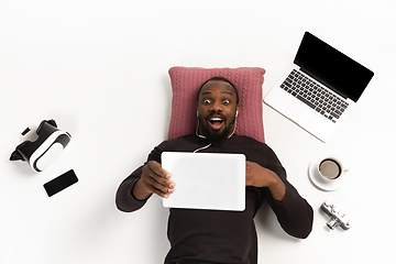 Image showing Emotional african-american man using tablet surrounded by gadgets isolated on white studio background, technologies connecting people. Shocked, scared