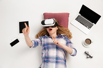 Image showing Emotional caucasian woman using VR-headsed, surrounded by gadgets isolated on white studio background, technologies. Touching